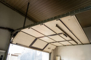 Interior View Of An Open Sectional Garage Door With Metal Tracks And Ceiling Panels, Showing Workshop Entrance And Overhead Mechanism.